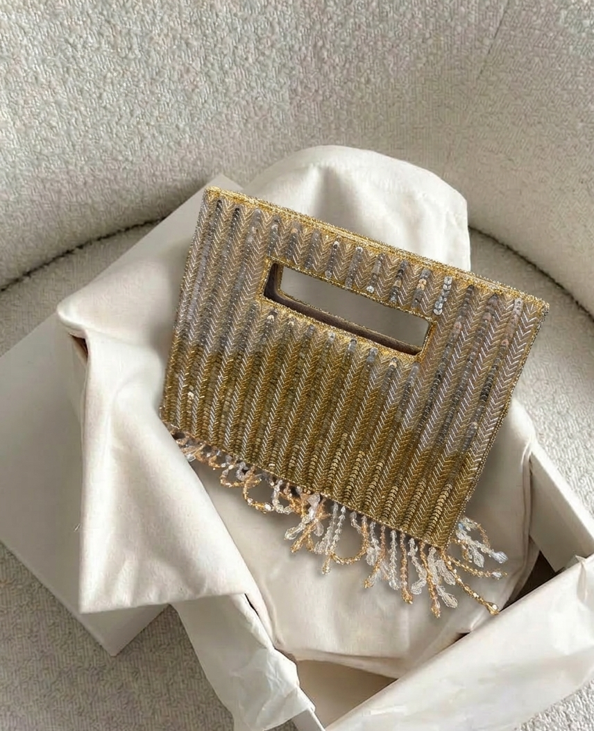 Gold beaded clutch bag with fringe on a white fabric background